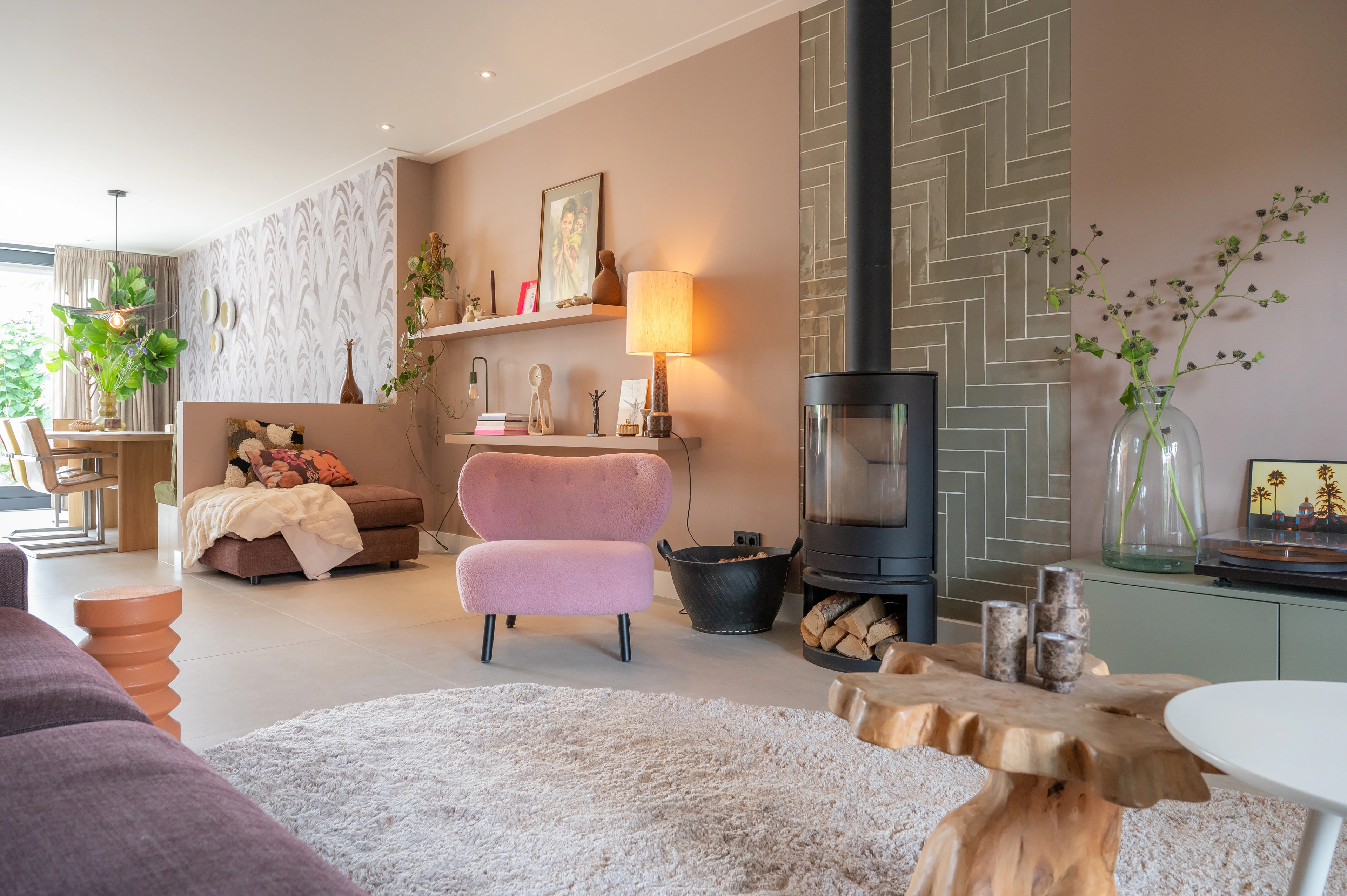 Woonkamer met roze fauteuil, houtkachel en warme kleuren